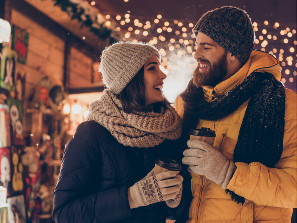 Couple at Christmas Market with hot drinks and twinkling lights in the background