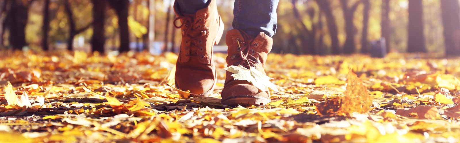 Close up of feet in boots walking on autumn leaves in a park