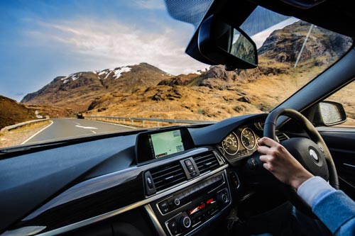Hand on steering wheel inside car looking out at Scottish Highlands scenery