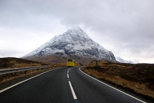 Yellow coach travelling along road to Glencoe Scotland