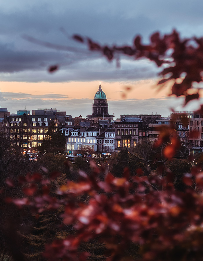 A view of Edinburgh at night with red Autumn leaves framing the picture
