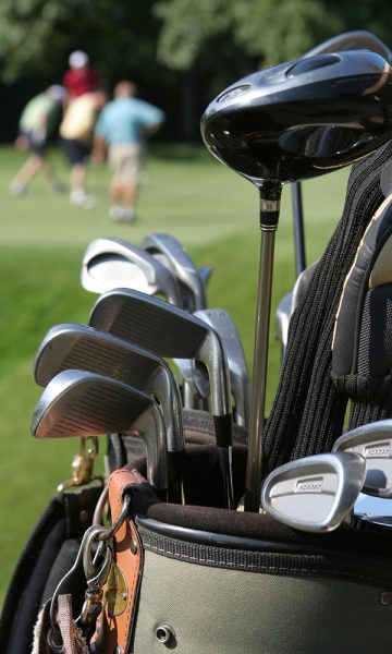 A close up of a golf bag with clubs in it and golfers playing golf in the bacground