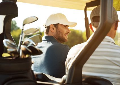 Two men in a golf buggy with their golf clubs