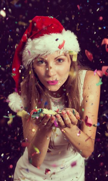 A girl in a Santa hat blowing Christmas confetti