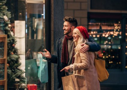 A couple looking in a shop window and smiling while Christmas shopping