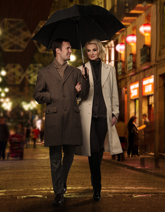 A romantic couple walking through a street at night arm in arm with an umbrella over them