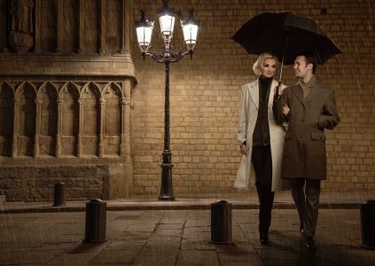 An elegant couple romantically walking through an old city at night with an umbrella over them
