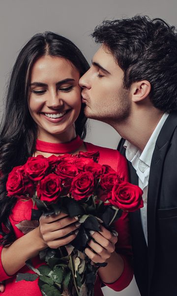 A girl with a bunch of roses being and being kissed by her partner