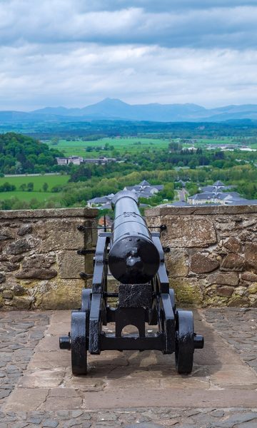 A canon pointing out across the walls of Stirling Castle to a long view beyond