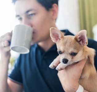A man cuddling a Chihuahua while drinking a hot drink