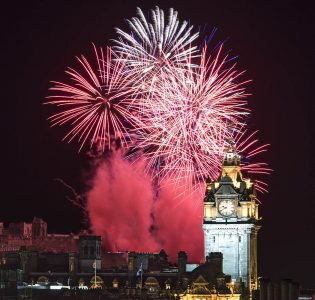 Mass of bright fireworks behind a clock tower at Edinburgh Hogmanay