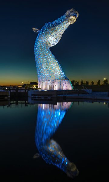 One of the Kelpies lit up at night with its reflection in the water