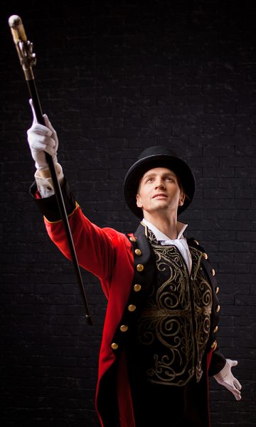 A theatrical showman with his arm and stick in the air