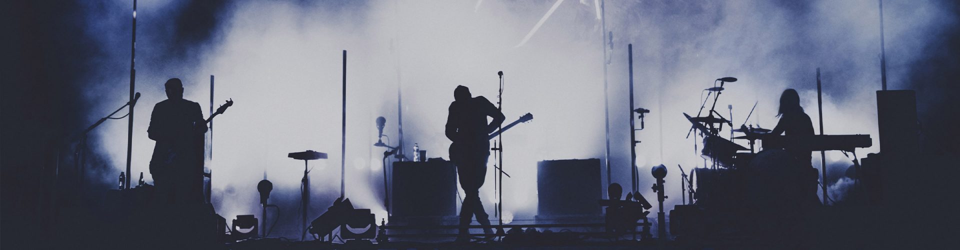 Silhouettes of a rock band performing on a smokey stage