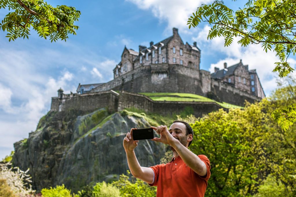 A tourist taking a selfie with Edinburgh Castle behind him