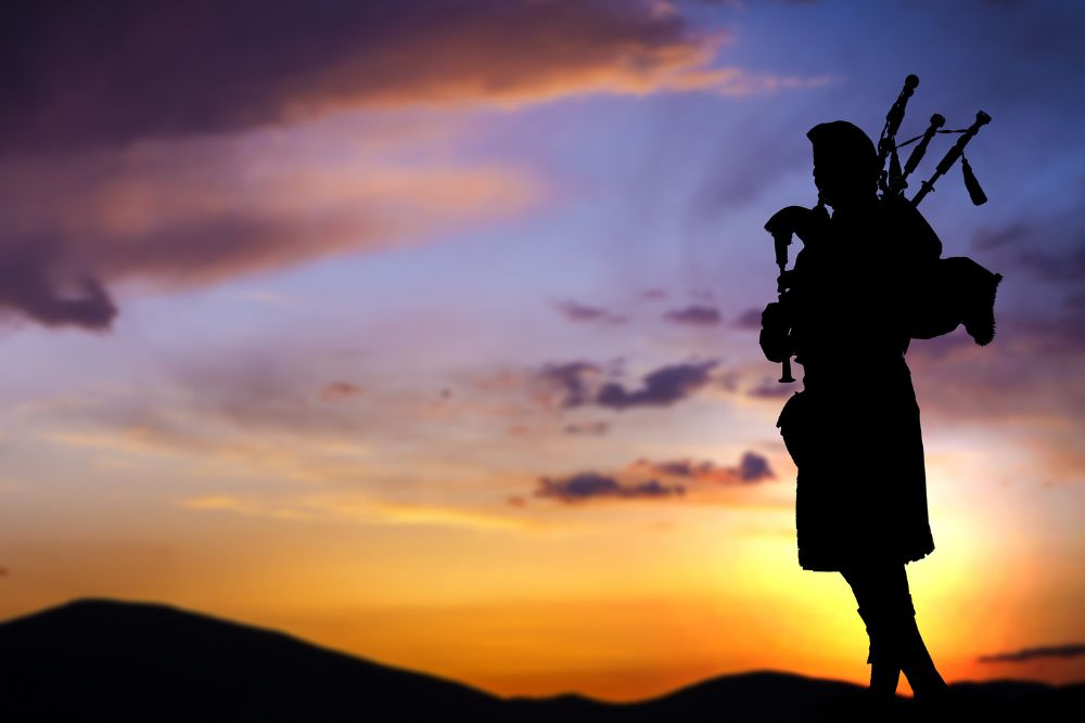 Bagpipe player in silhouette against dramatic sunset sky.